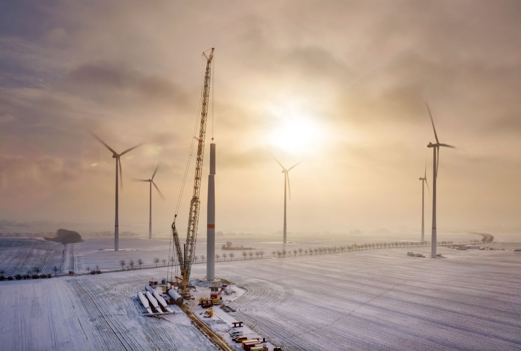 Lattice boom crane assembling a wind turbine in a snow-covered landscape